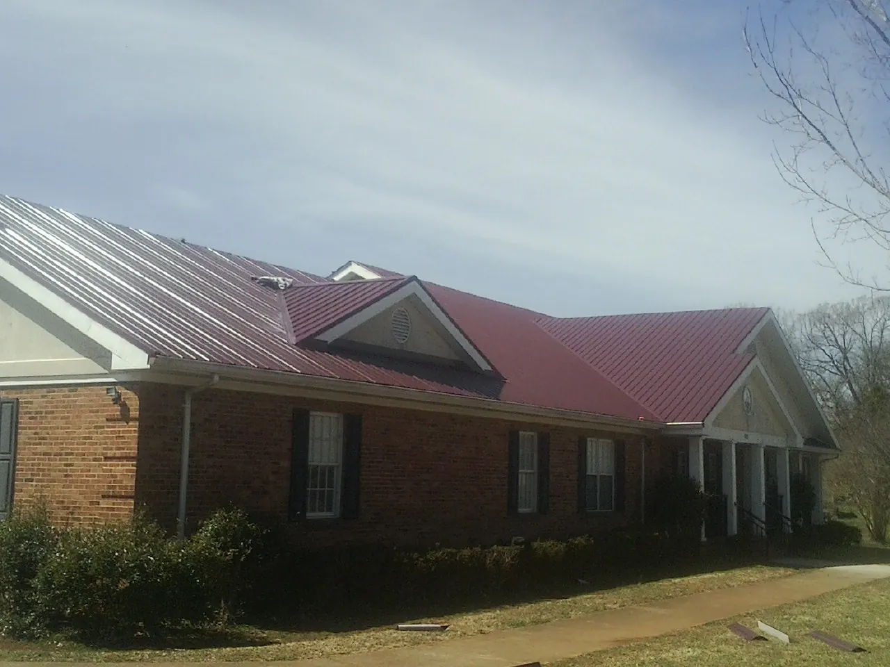 Red metal roof with gabled entries on a long brick building, from a Hail Damage Roof Repair job in Westfield